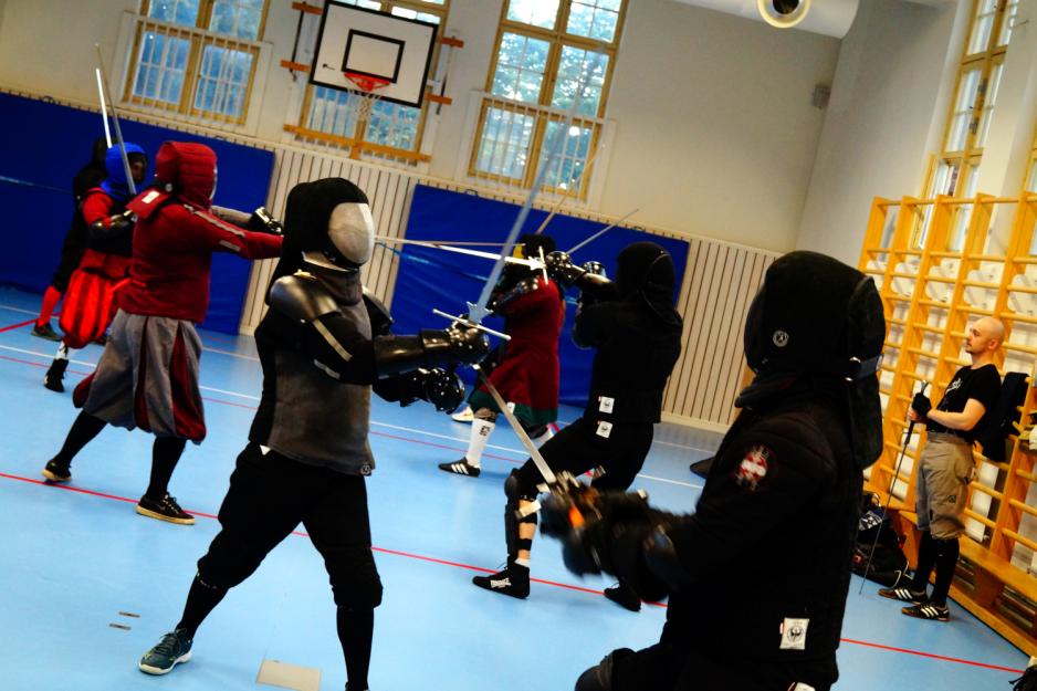Fekterne sparrer i gymsalen, Marcus observerer fra sidelinjen