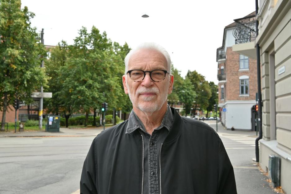 Frank H&oslash;if&oslash;dt som poserer p&aring; gata foran bilvei, gr&oslash;nne tr&aelig;r og gr&aring; himmel.