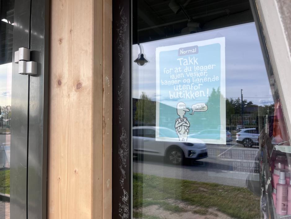 P&aring; bildet ser vi en plakat som har blitt hengt opp utenfor Normalbutikken. P&aring; plakaten st&aring;r det "Takk for at du legger igjen vesker, bagger og lignende utenfor butikken!"