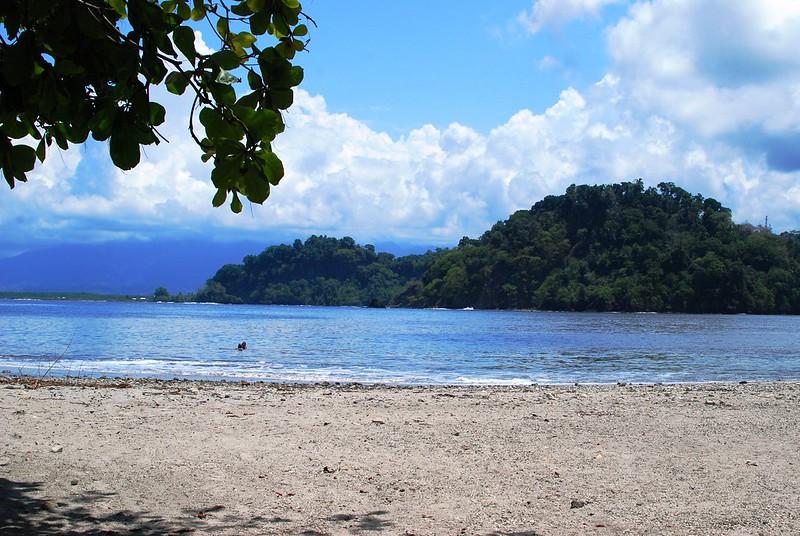 En sandstrand vendt ut mot havet i Costa Rica. Ute i havgapet ser vi en skogkledd øy.