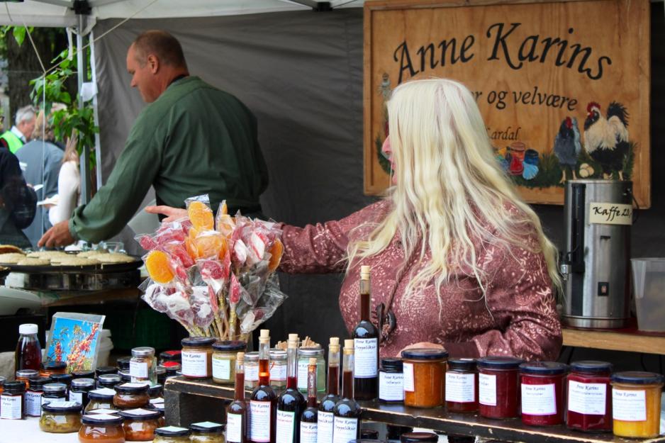 Anne Karin Bodahl er fotografert i salgsboden sin. Foran henne står et utvalg av varene hun selger. 