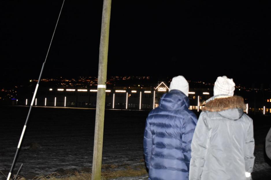 En mann og en dame i vinterklær står med ryggen til fotografen og ser bort på en bygning som lyser sterkt.
