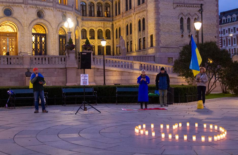 Noen snakker i mikrofon foran Stortinget foran lys på bakken, formet som et hjerte.