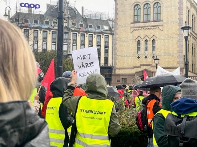 Demonstranter står med ryggen til, og vi ser en plakat det står "møt våre krav" på.