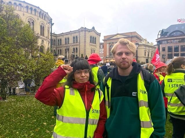 Dame står med hånden hevet og knyttet sammen med mann, foran stor folkemengde i demsonstrasjon.