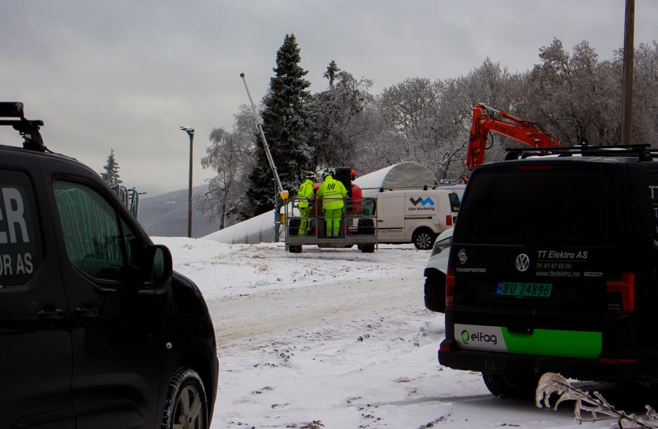 To bygningsarbeidere står i en kran. Kranen befinner seg øverst i en slalåmløype ved Tryvannstårnet.