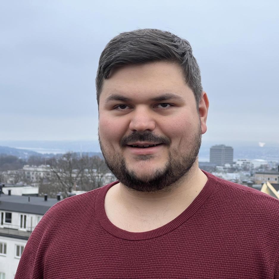 Portrett av Christian Thon fra Blindeforbundet. Han står ute foran den blå himmelen, og har på seg en rød genser. Han har mørkt hår, og smiler mot kamera.