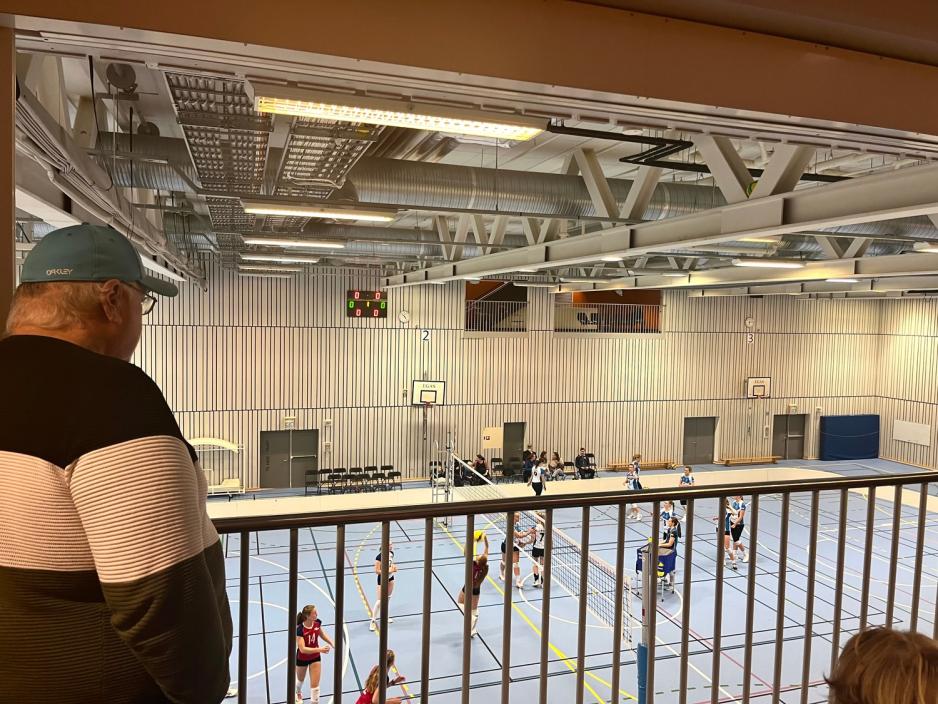 Ryggen til mann som ser utover gymsal hvor det varmes opp til volleyballkamp