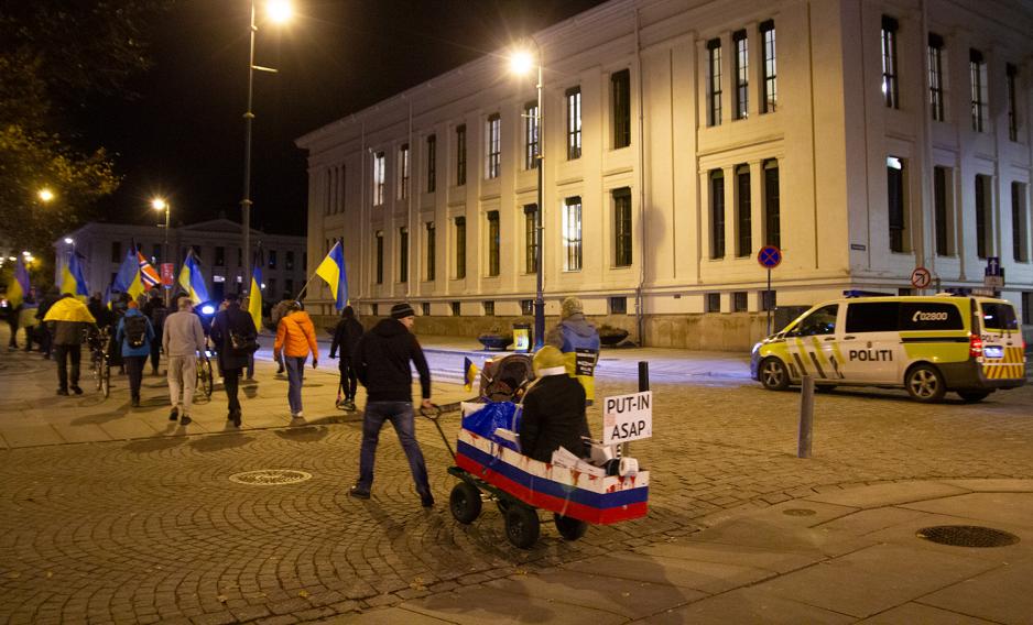 Demonstranter med ukrainske flagg beveger seg oppover Karl Johan, med en politibil ved siden av. 