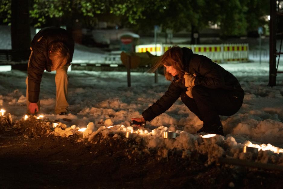 Kvinne sitter på huk og tenner på fakler i mørket