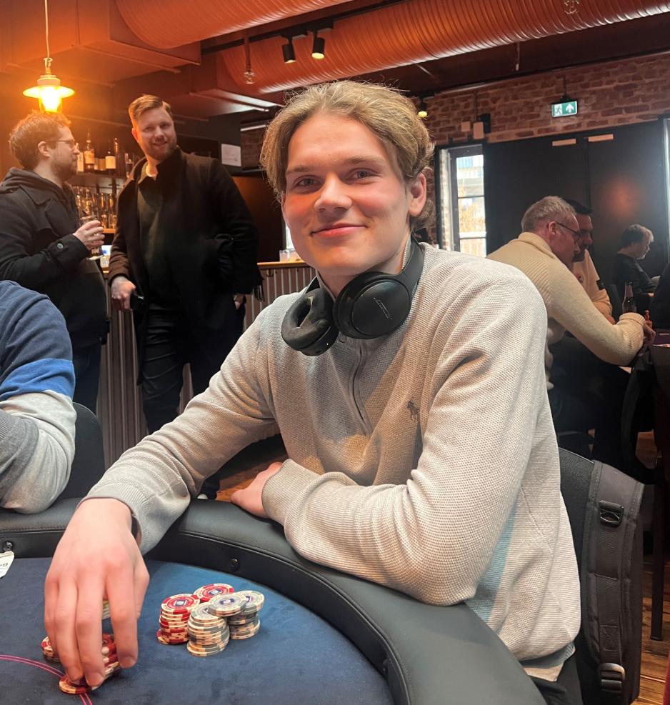 Smilene ung mann i grå genser og hodetelefoner rundt nakken, sitter ved et bord og spiller poker.