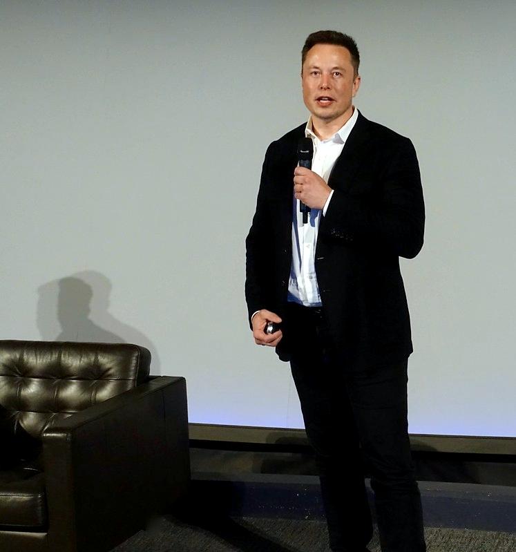 Elon Musk står i dress og snakker i en mikrofon.