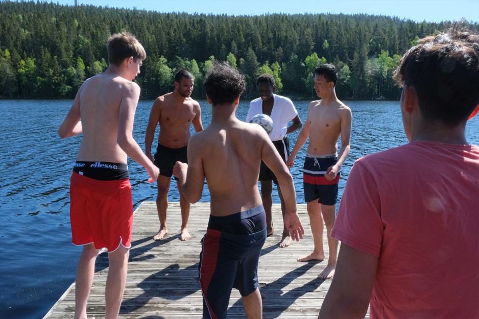 Seks unge gutter står i ring på flytebrygge og spiller enspretten med ball.