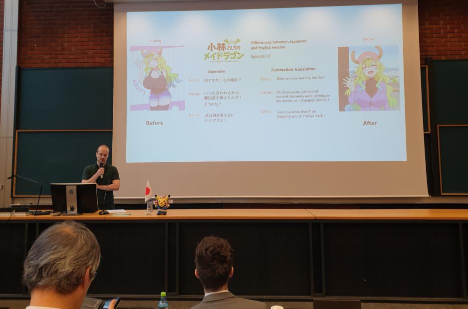 Mann står på et podie og taler foran en power point med bilde av en anime jente