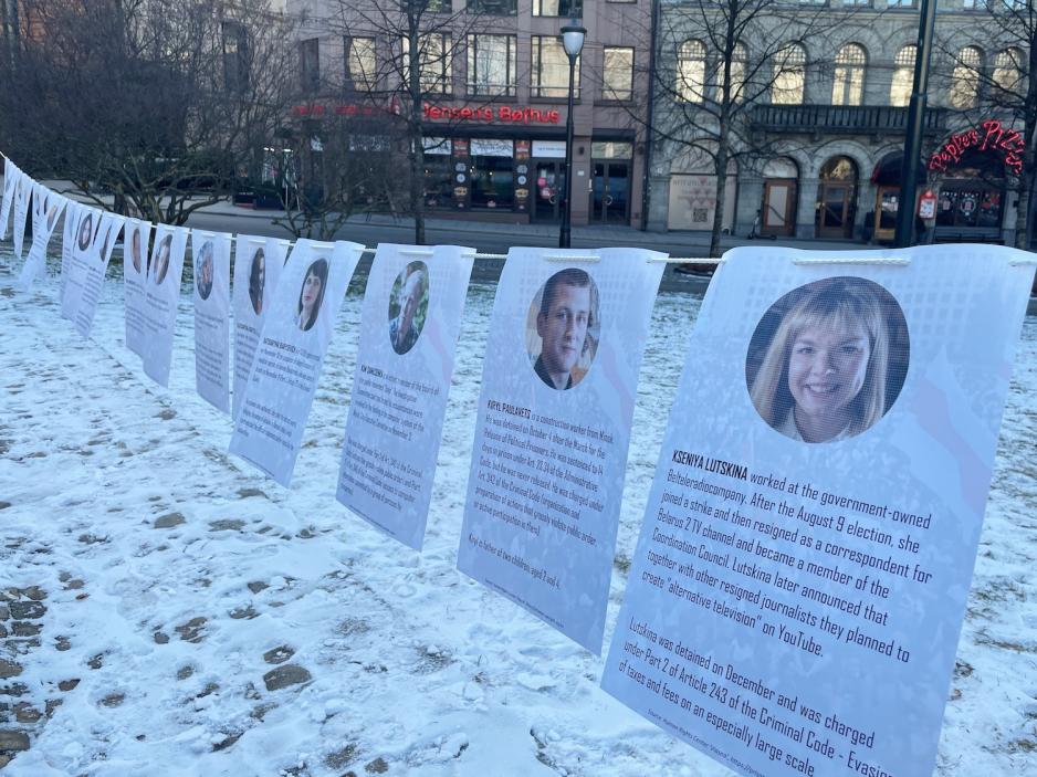 Remse hengt opp på stang med flere A4 ark, der fengslede demonstranter fra Hviterussland er avbildet.