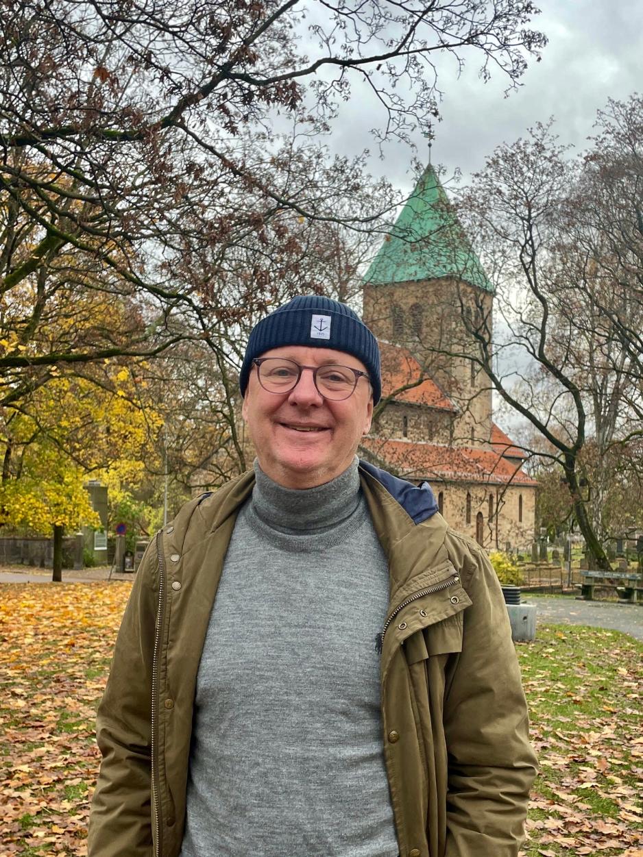 Bildet viser Finn Folke, som er kommunikasjonsansvarlig i Det kirkelige fellesrådet i Oslo. Han har på seg briller og lue, og er avbildet foran Gamle Aker kirke på St Hanshaugen i Oslo. 