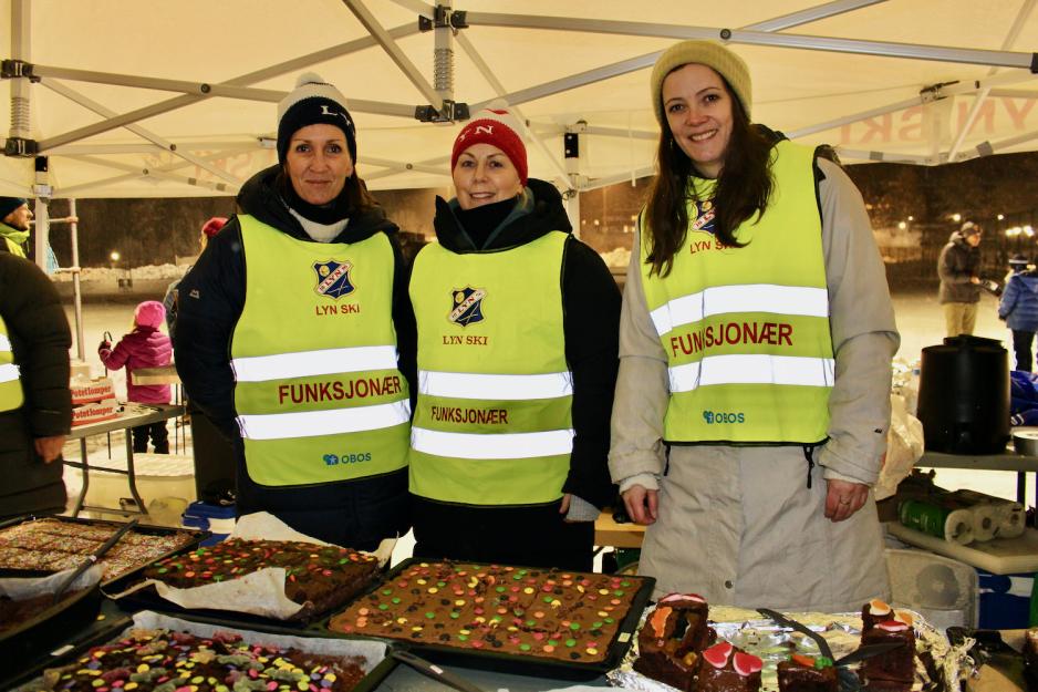 Tre damer står foran et kakebord på et skirenn.