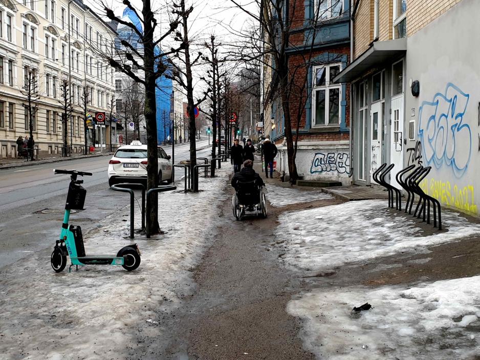 Håkon Bjar beveger seg nedover gata i rullestol. Gatekanten er dekket av is og snø.