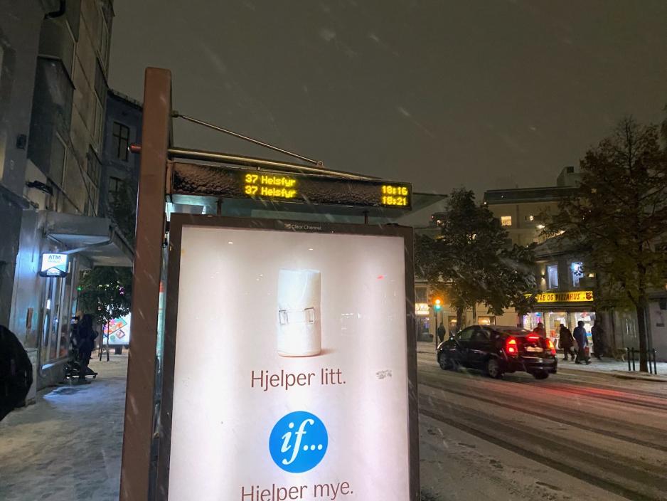 Bildet viser buss-stoppet i Tøyengata i retning 37-Helsfyr. Det er en "if"-reklame, som sier at "if ... hjelper mye". Det er en bil som kjører forbi. Det er mørkt ute, og snøen faller.