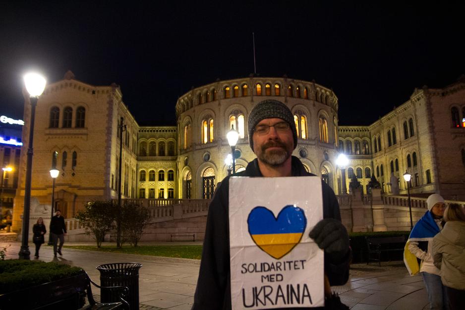 En mann står med et skilt foran seg, foran Stortinget. 