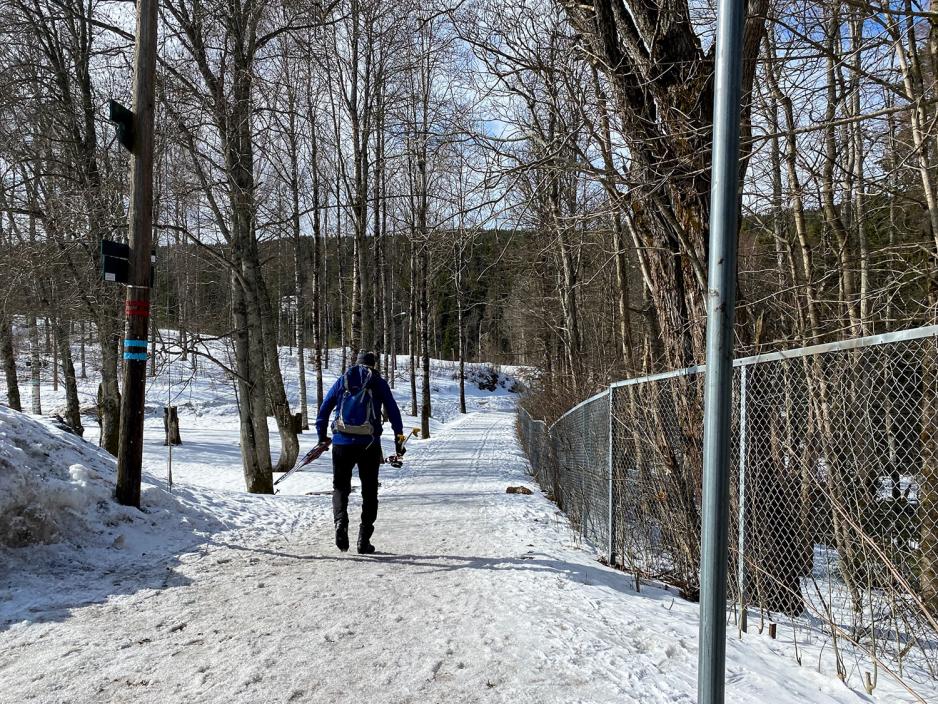 Mann med skiutstyr i hendene går inn i løypa