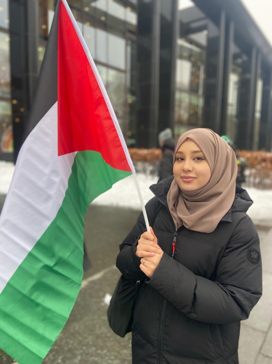 Et portrettbilde av Bibi Fatima Musavi som veiver med et palestinsk flagg. Hun smiler til kameraet. 