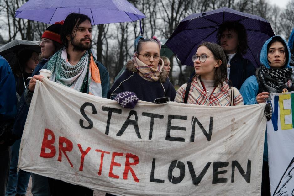 Tre stykker holder et demonstrasjonsbanner hvor det står "Staten bryter loven"