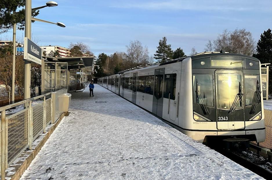 T-banen ankommer stasjonen på Kalbakken. Flere personer står på perrongen. 