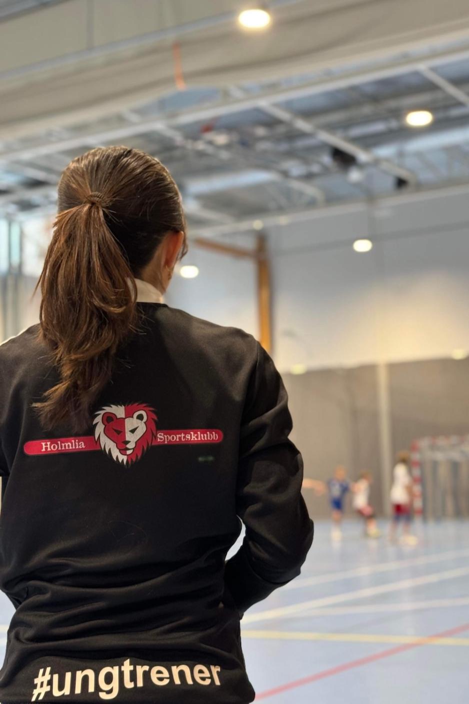 Katrina Lu med Holmlia sportsklubb jakke med ung trener på ryggen i håndballhallen