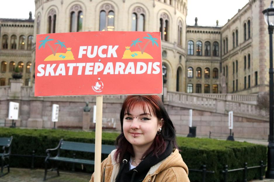 En jente som holder en plakat der det står "F*** skatteparadis"