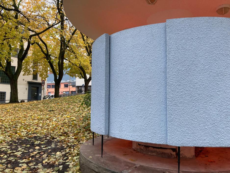 Halvnært bilde av Kjærlighetskarusellen med inngangen til urinalen i fokus. Kulturminnet er gråmalt.
