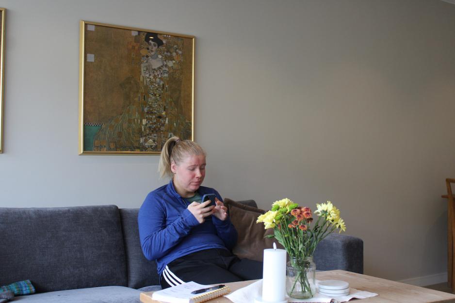 Kristin Hauglid sitter med telefonen i henda, og scroller på mobilen. Hun sitter i sofaen i stua.