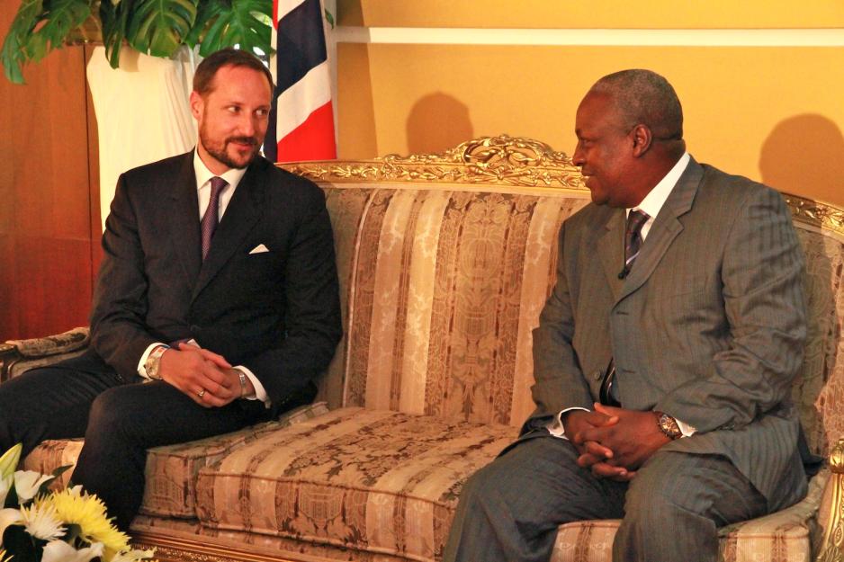 vi ser kronprins håkon og john mahama sitte i en sofa. De smiler mot hverandre. I bakgrunnen ser vi et norsk flag. 