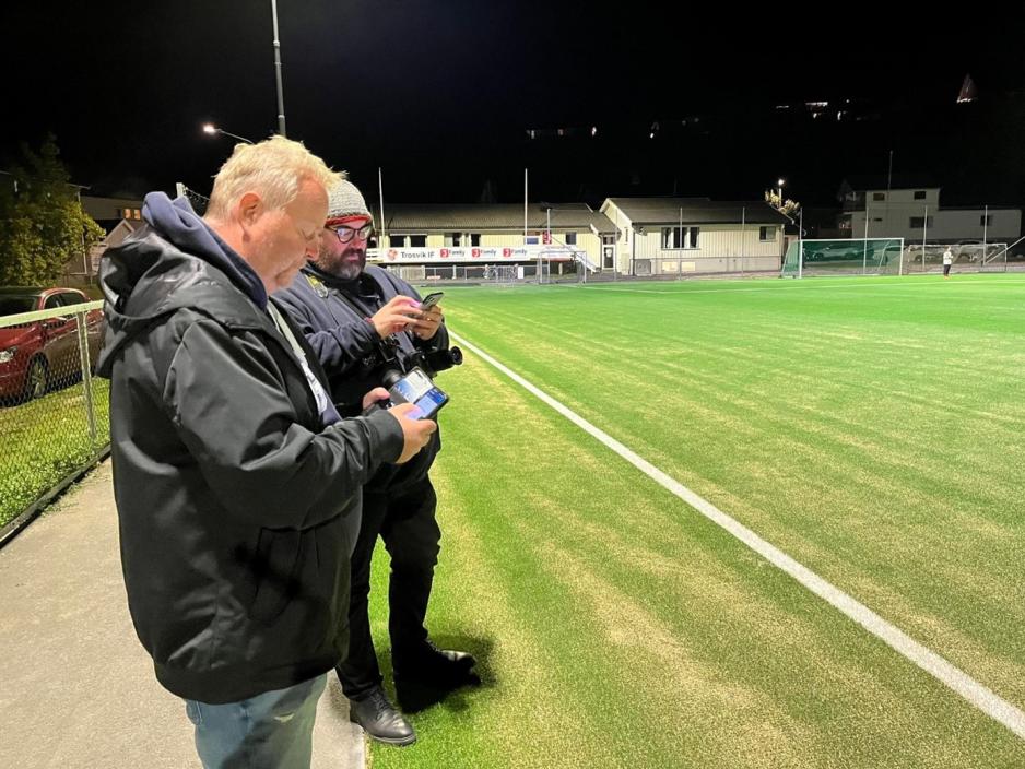 Marius Helgå og Trond Sæterøy noterer på mobiltelefonene langs sidelinja. Banen er i bakgrunnen.