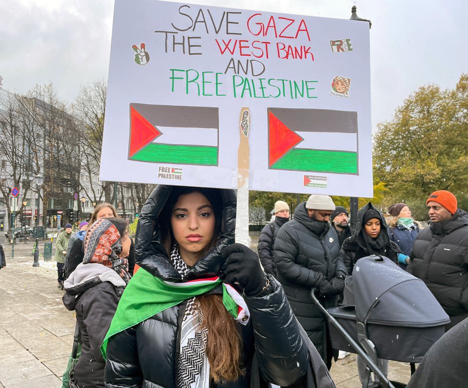 Naya Ikram El Habbach holder et skilt der det står "Save Gaza, the west bank, and free Palestine"