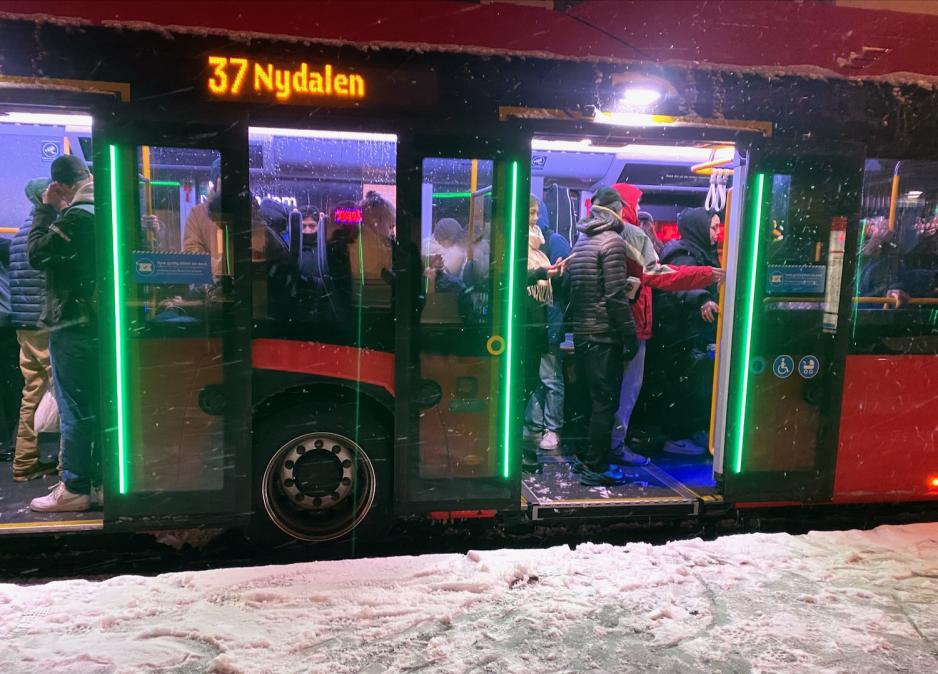 Full buss med passasjerer i linje 37 mot Nydalen. Det snør utenfor, og er snø på bakken. Passasjerene må stå på bussen, da det ikke er sitteplasser. 