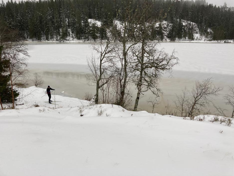 Bildet er av et vann ved Skjennungsvolden. Det er snø, og en person fyker forbi på ski langs vannet. 