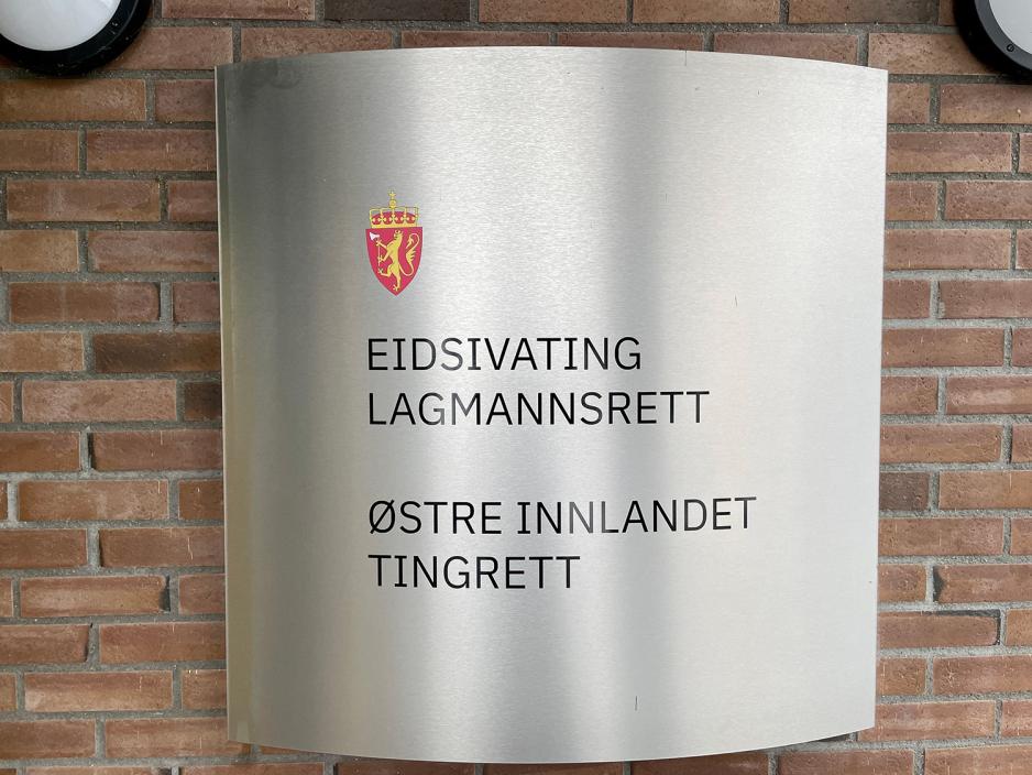 Man ser et skilt i polert metall som henger på en murvegg. På skiltet er det bilde av riksvåpenet. Det står at det er Østre Innlandet Tingrett, samt Eidsivating Lagmannsrett.