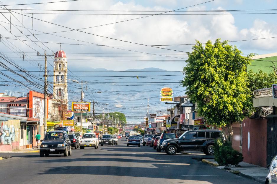 Trafikkert vei i San José i Costa Rica. Mange biler, lave forretningslokaler og tet-i-tett med telefonledninger.