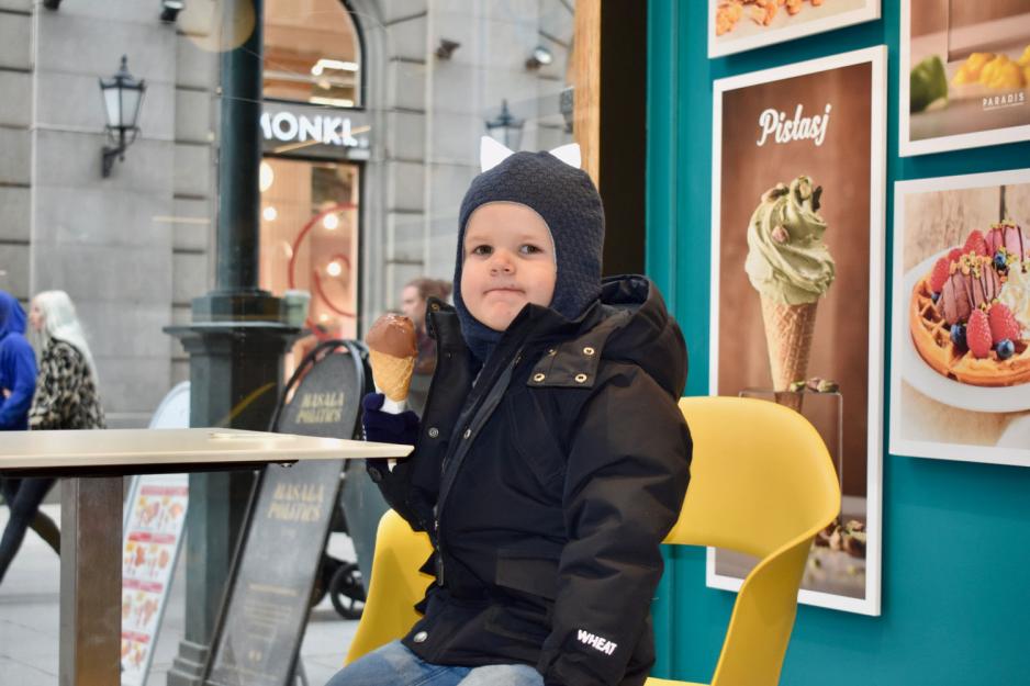 Liten gutt spiser sjokoladeis i kjeks. Han har på seg mørkeblå vinterjakke og mørkeblå lue. 