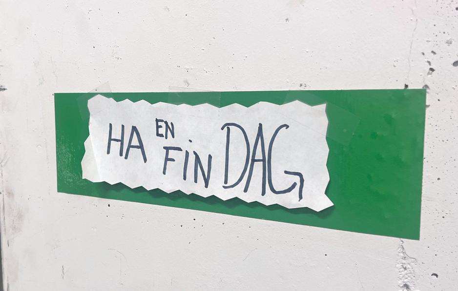 Bilde av et skilt på en vegg der det står "Ha en fin dag". 