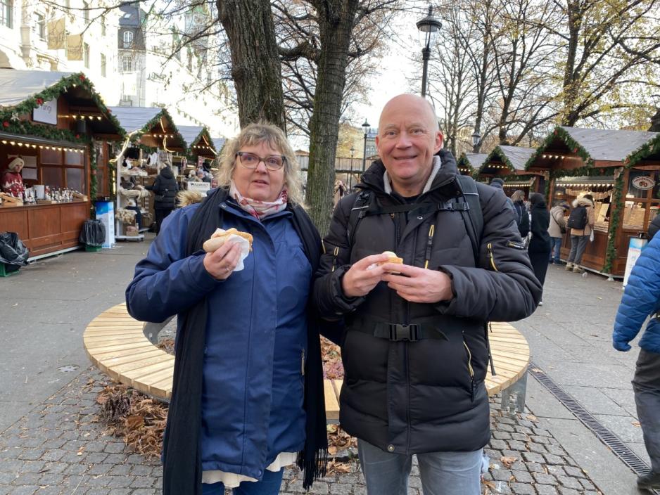 Et dansk ektepar står og spiser pølser på et julemarked på Karl Johan. 