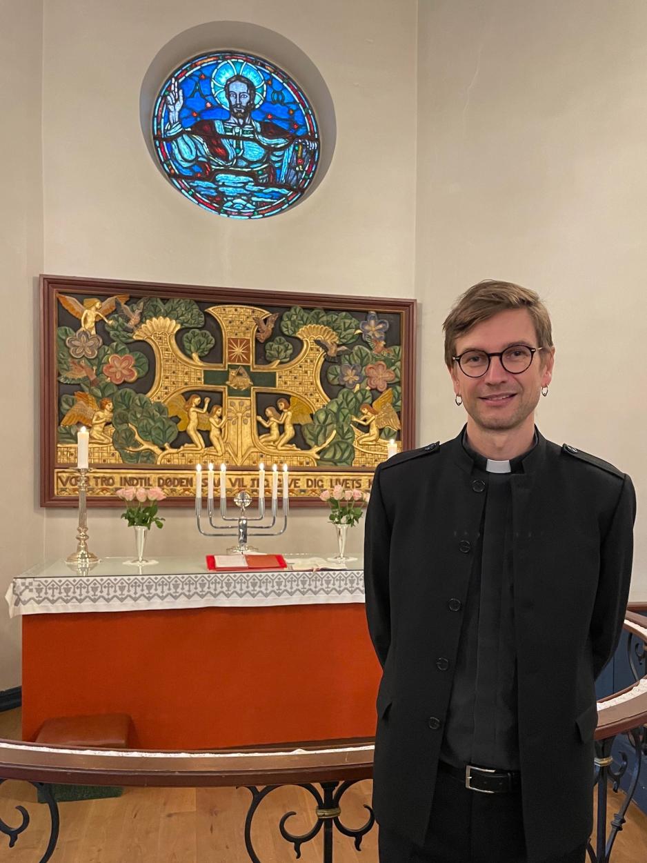 Bildet viser han som er prest i Røa og Sørkedalen menighet. Han står foran alteret i Sørkedalen kirke, og på alteret er det lysestaker og rosa blomster.<