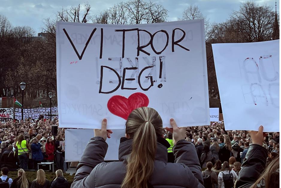 En jente holder opp et skilt der det står "Vi tror deg"