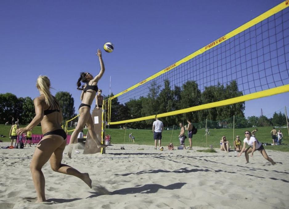 Kritkamchon spiller sandvolleyball. Hun hopper og er på vei til å slå ballen over det gule nettet.