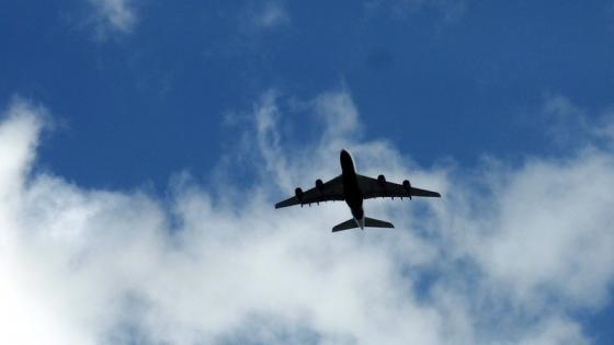 Bilde av et fly tatt underfra, blå himmel og skyer i bakgrunnen.