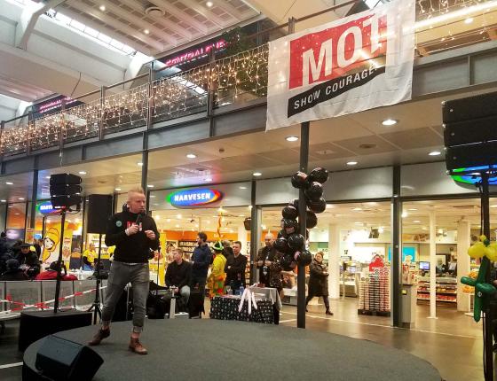 Konferansier for "Mot til å glede-dagen" står på scenen foran Narvesen på Oslo S.