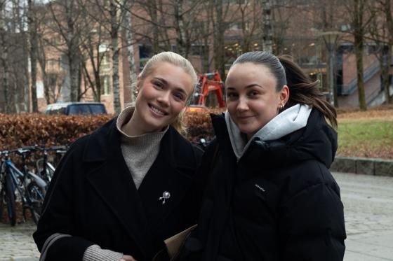 To damer som står vedsiden av hverandre og smiler, med en plen i bakgrunnen