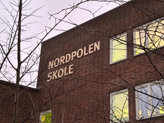 Bide av Nordpolen skole med litt tre uten blader på siden. Vi ser godt nordpolen skole skiltet