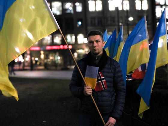 Rostyslav Yevdiukhin står på Eidsvoll plass mens han holder en flaggstang med et Ukrainsk flagg